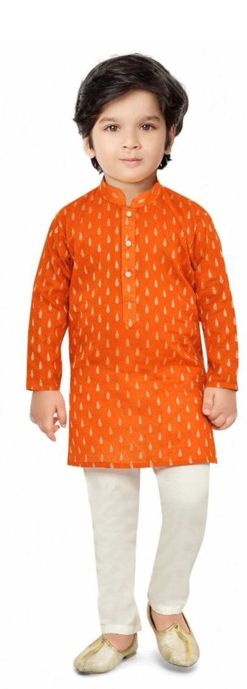 May include: A young boy wearing a long-sleeved orange kurta with a white pattern and white trousers. He is wearing gold shoes.