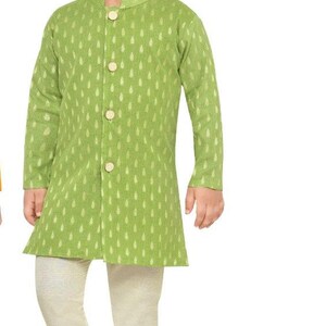 May include: A young boy wearing a green kurta with a gold leaf pattern and white trousers. He is wearing gold shoes.