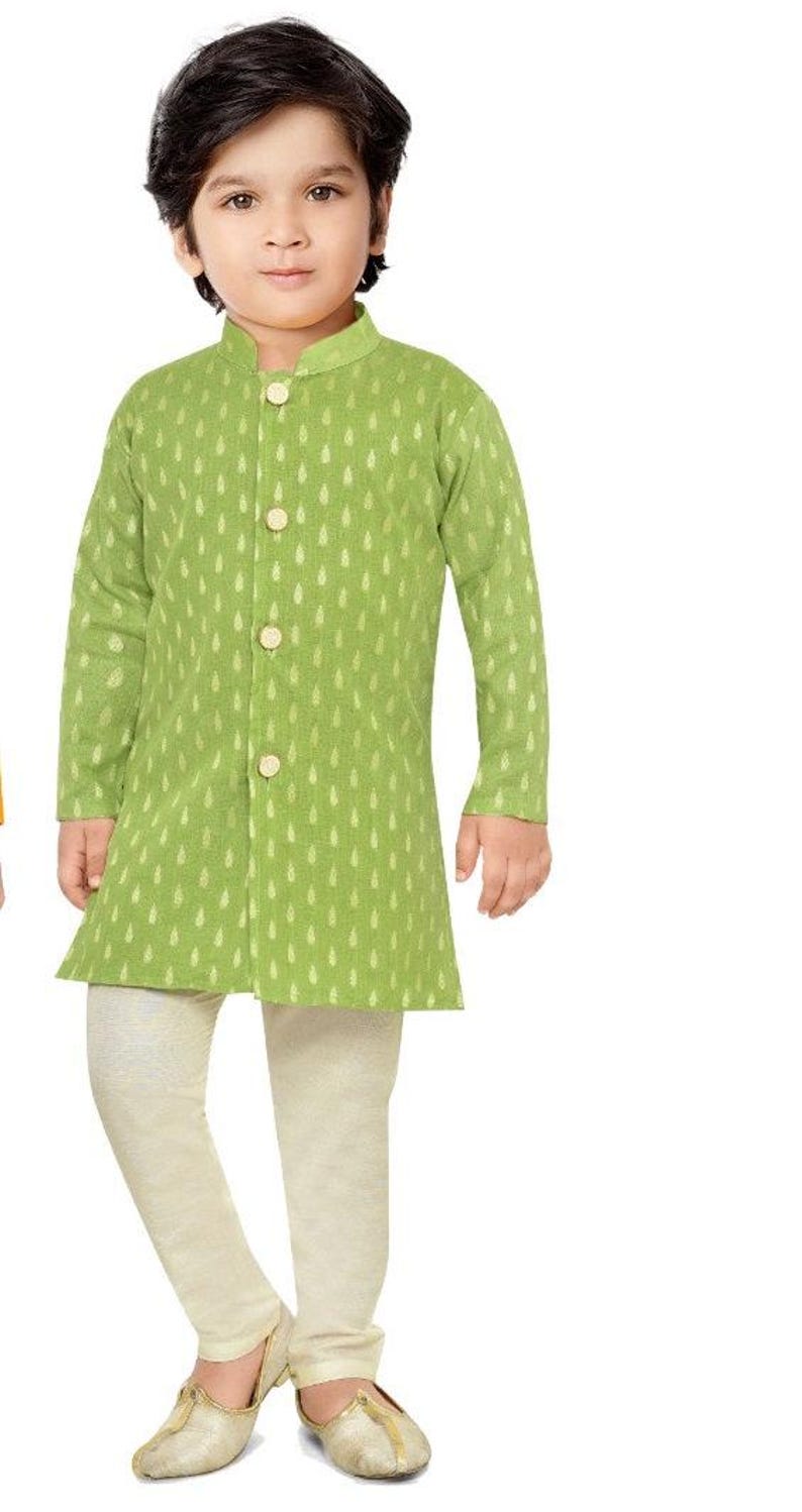 May include: A young boy wearing a green kurta with a gold leaf pattern and white trousers. He is wearing gold shoes.
