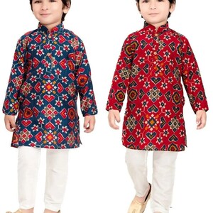 May include: Two young boys wearing traditional Indian clothing. The boys are wearing long-sleeved shirts with a geometric pattern and white pants. The shirt on the left is blue with red, yellow, and white patterns. The shirt on the right is red with blue, yellow, and white patterns.