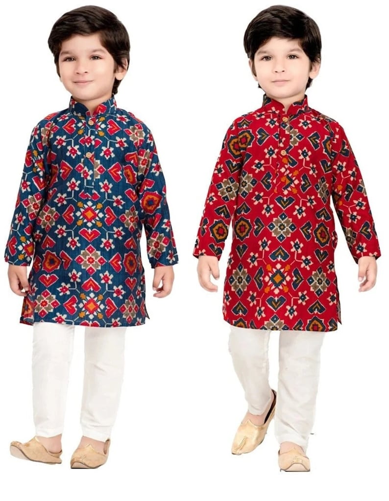 May include: Two young boys wearing traditional Indian clothing. The boys are wearing long-sleeved shirts with a geometric pattern and white pants. The shirt on the left is blue with red, yellow, and white patterns. The shirt on the right is red with blue, yellow, and white patterns.