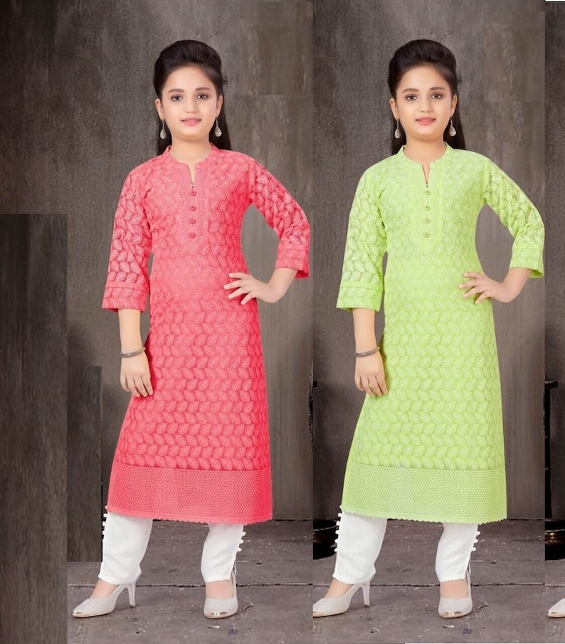 May include: Two girls wearing matching long-sleeved, embroidered kurtas with white pants and white shoes. One kurta is pink and the other is green.