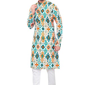 May include: A white long-sleeved shirt with a geometric pattern in shades of teal, orange, and brown. The shirt has a mandarin collar and a button closure. The model is wearing white trousers and brown shoes.