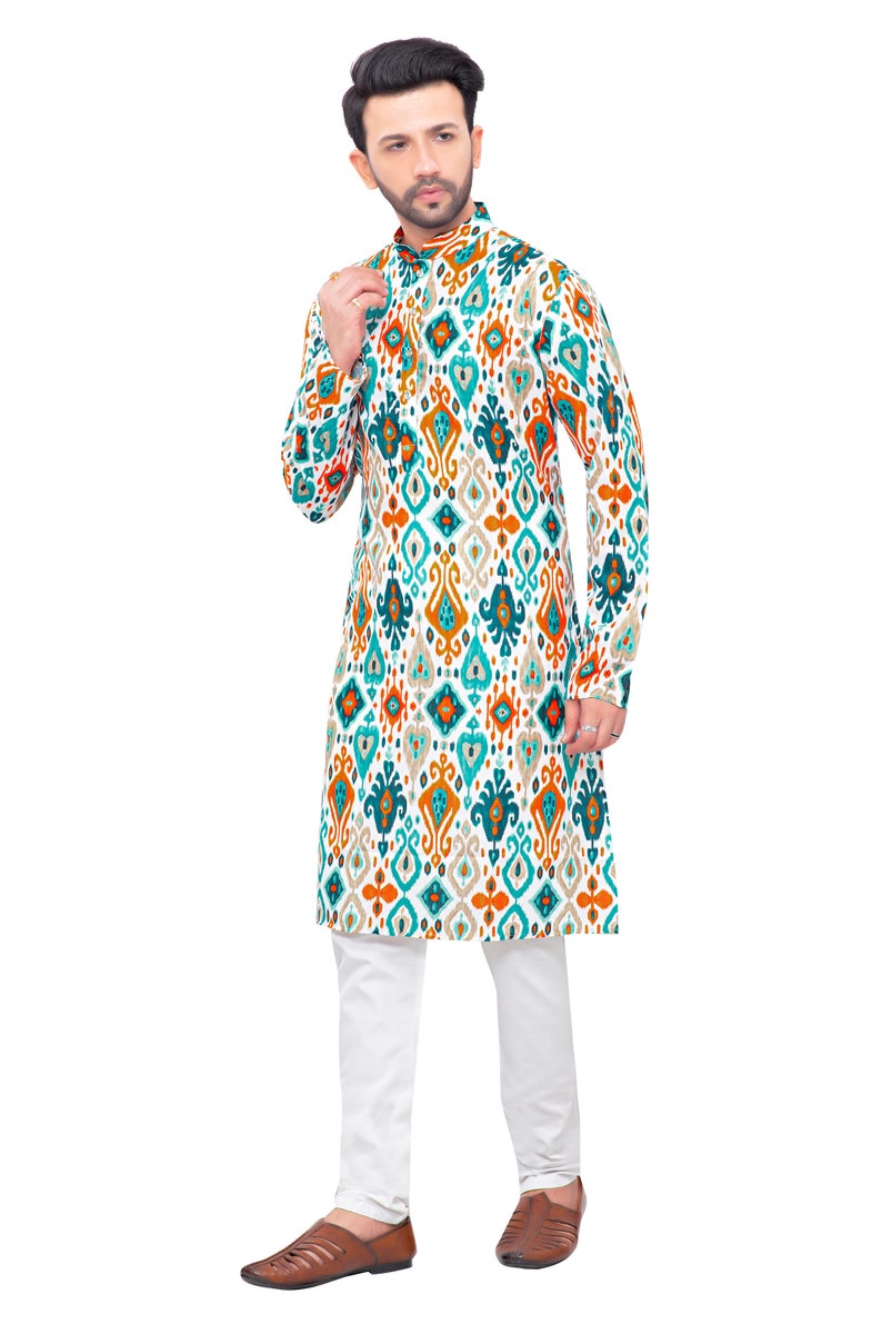 May include: A white long-sleeved shirt with a geometric pattern in shades of teal, orange, and brown. The shirt has a mandarin collar and a button closure. The model is wearing white trousers and brown shoes.