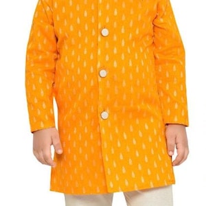 May include: A young boy wearing a yellow kurta with a white pattern and white trousers. He is wearing white shoes.