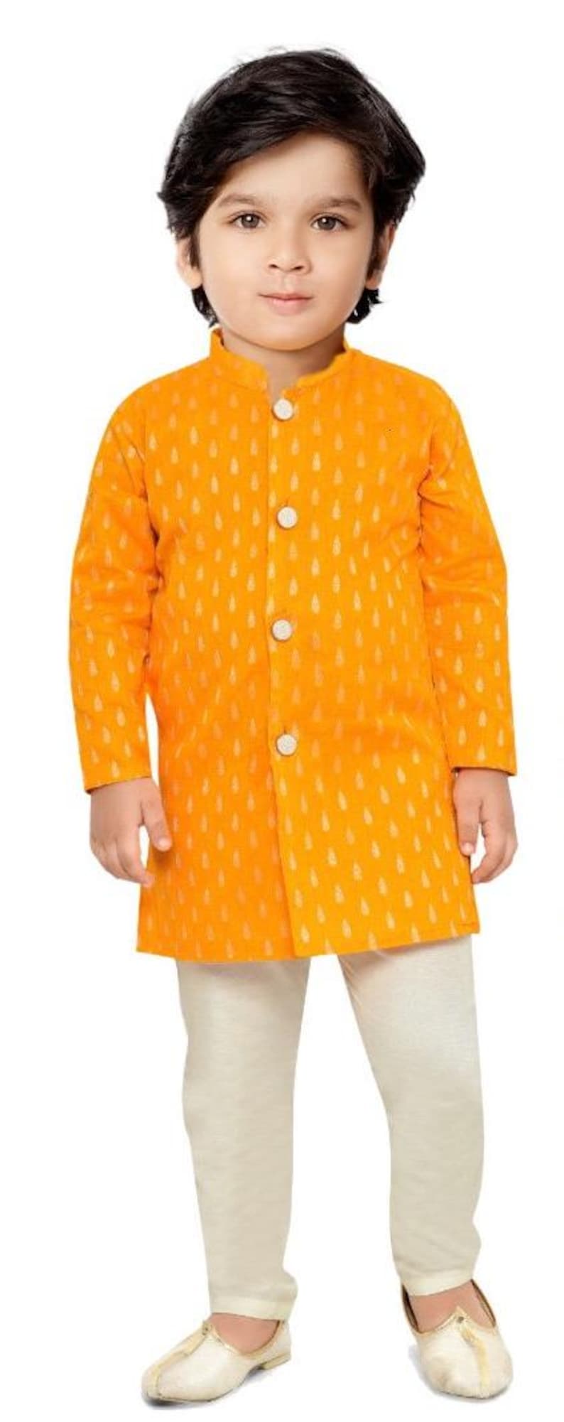 May include: A young boy wearing a yellow kurta with a white pattern and white trousers. He is wearing white shoes.