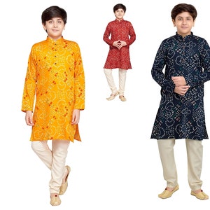 May include: Three boys wearing traditional Indian clothing called kurtas. The kurtas are in different colors and patterns: yellow with red dots, red with white dots, and blue with white dots. The boys are wearing white pants.