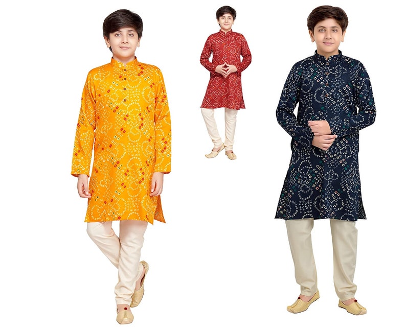 May include: Three boys wearing traditional Indian clothing called kurtas. The kurtas are in different colors and patterns: yellow with red dots, red with white dots, and blue with white dots. The boys are wearing white pants.