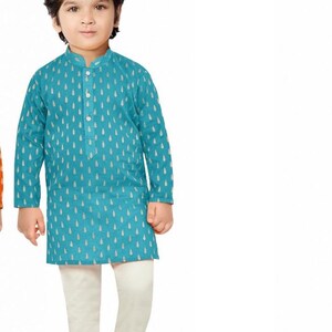 May include: A young boy wearing a teal blue kurta with a white pattern and white trousers. He is wearing gold shoes.