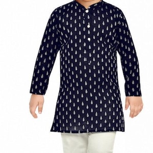 May include: A young boy wearing a navy blue long-sleeved shirt with a white teardrop pattern and white trousers. He is wearing gold shoes.