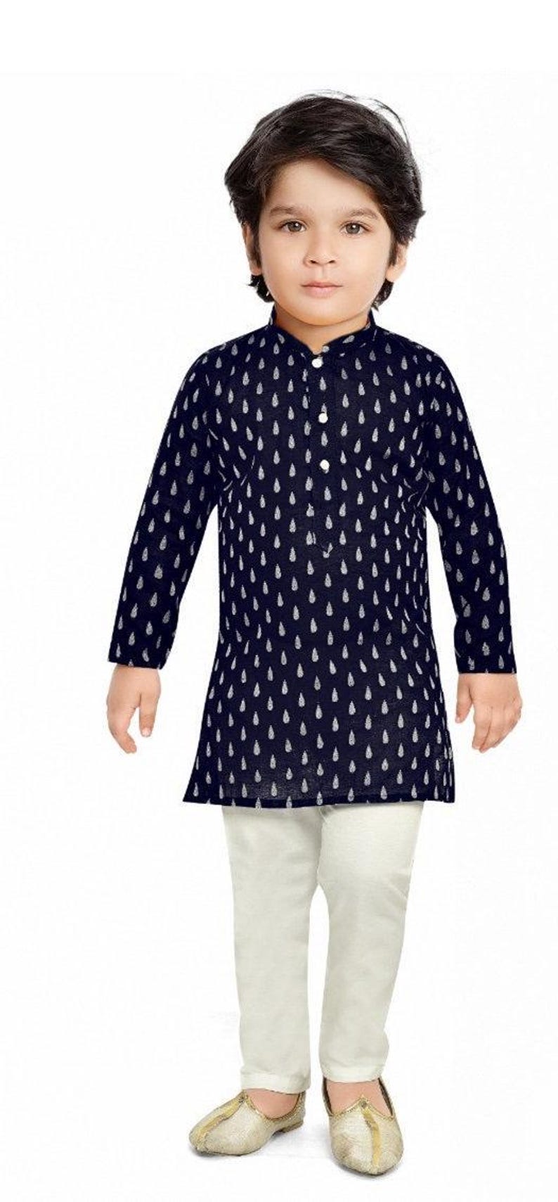 May include: A young boy wearing a navy blue long-sleeved shirt with a white teardrop pattern and white trousers. He is wearing gold shoes.