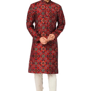 May include: A red long-sleeved kurta with a geometric pattern. The kurta has a mandarin collar and a button closure. The model is wearing white pants and brown shoes.