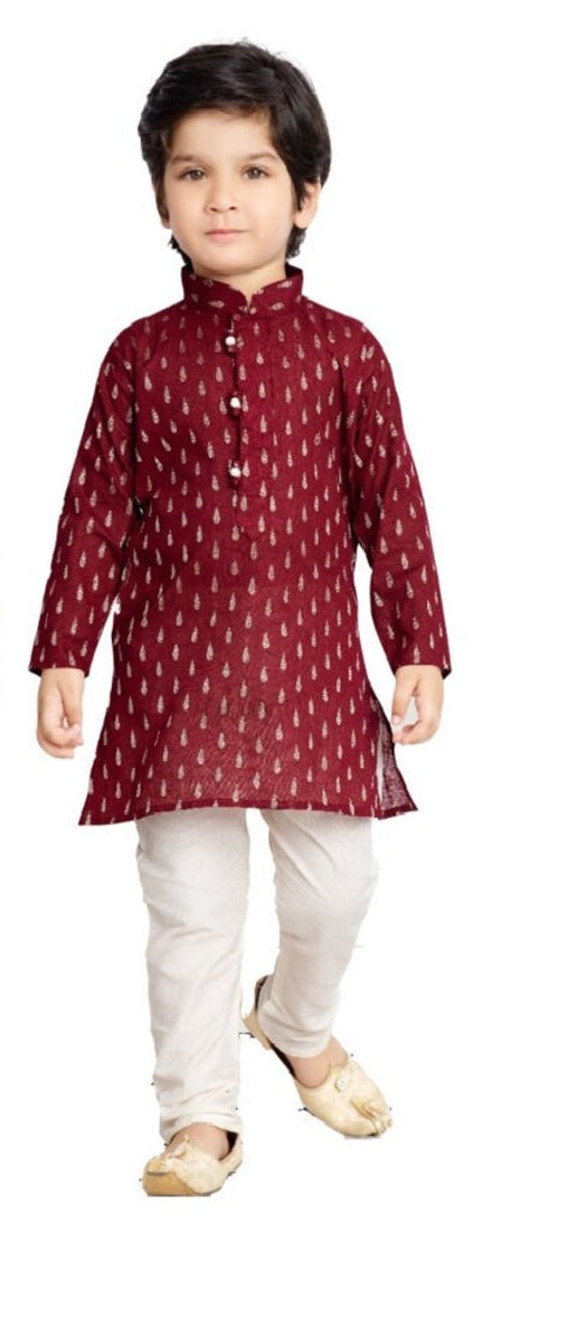 May include: A young boy wearing a maroon kurta with a white print and white trousers. He is wearing white shoes.