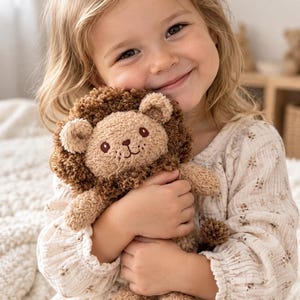 Può includere: Un leone di peluche realizzato in filato testurizzato color marrone chiaro e scuro. Il giocattolo presenta un viso rotondo, piccole orecchie arrotondate e una folta criniera riccia marrone scuro. Ha occhi, naso e bocca ricamati in marrone.