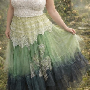 May include: A white lace camisole top with thin straps paired with a long, layered tulle skirt. The skirt features a gradient color palette transitioning from light lime green at the waist to a deep forest green and dark charcoal at the hemline.