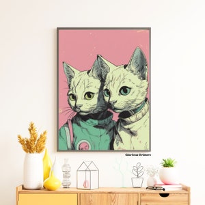 May include: A digital art print featuring two white cats with green eyes wearing astronaut suits. The cats are against a pink background with the text "Glorious Critters" at the bottom.