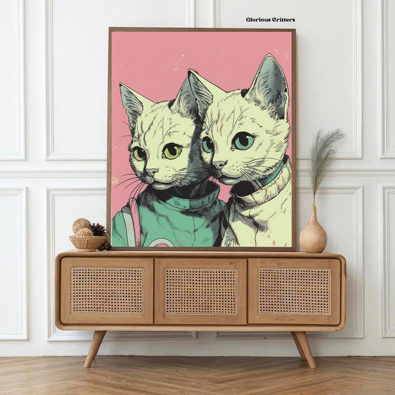 May include: A framed print of two cats wearing astronaut suits. The cats are white with green and blue eyes. The background is pink with white stars. The print is titled "Glorious Critters".