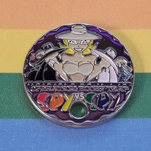 May include: A round, metal pin with a purple background. The pin features a cartoon woman wearing a white hat and a white top. The text "SPY VS SPY" is written in rainbow colors around the edge of the pin.