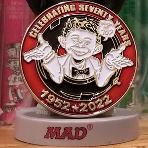 May include: A collectible figurine of Alfred E. Neuman, the mascot of Mad magazine, celebrating 70 years. The figurine features a smiling face with a missing tooth, wearing a black suit and red bow tie. The base reads "Celebrating Seventy Years 1952-2022 MAD".