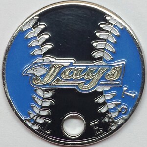 May include: A silver metal baseball-themed token with a blue and black enamel design. The token features the word "Jays" in a gold script font. The token has a hole in the center.