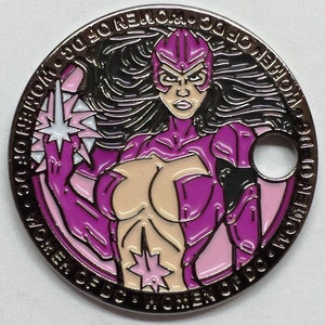 May include: A purple and pink metal disc with a woman superhero character in a purple suit and a star on her chest. The text around the edge reads "Women of DC & Women of  DC,  Welcome to the  Women of DC".