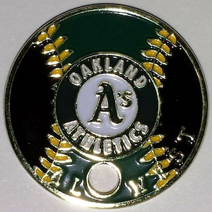 May include: A gold-colored metal Oakland Athletics baseball team coin with a green and black background. The coin features the team's logo, "Oakland Athletics", and a baseball stitch design.