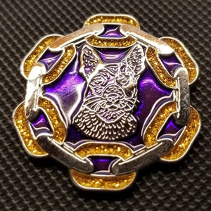 May include: A silver-toned pin with a purple and gold enamel design. The center features a detailed image of a dog's head. The pin is shaped like a Celtic knot.