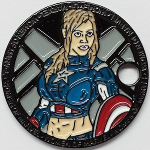 May include: A black and silver metal coin with a colorful image of a woman in a blue and red costume. The woman is holding a red, white, and blue shield. The coin has the text "Women of Marvel" and "S.H.I.E.L.D." around the edge.