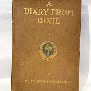 May include: A vintage book titled "A Diary From Dixie" by Mary Boykin Chesnut. The cover is a faded brown with gold lettering and a gold emblem featuring a tree and crescent moon. The book's edges show signs of wear.