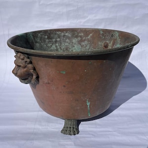 May include: A large copper planter with a lion head handle and three feet. The planter has a green patina and is in good condition.