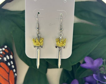 May include: A pair of silver dangle earrings with a gold crown and sword design.