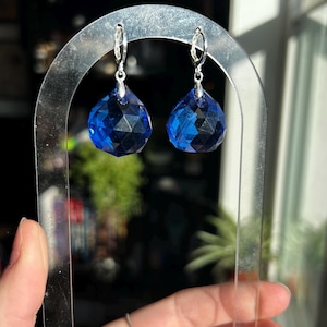 May include: A pair of silver hoop earrings with a faceted blue crystal drop on each earring.