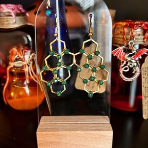 Op de afbeelding: Gouden oorbellen met een geometrisch honingraatontwerp en groene glazen kralen.