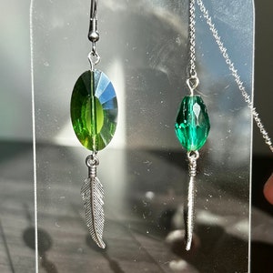 May include: A pair of green crystal earrings with silver feather charms hanging from a silver chain.