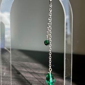 May include: A silver chain earring with a green crystal and a silver feather charm.