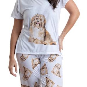 Puede incluir: Pijama blanco con estampado de perro marrón y blanco. La parte superior tiene manga corta y cuello redondo. El pantalón tiene un corte holgado y un estampado de perro por todas partes.