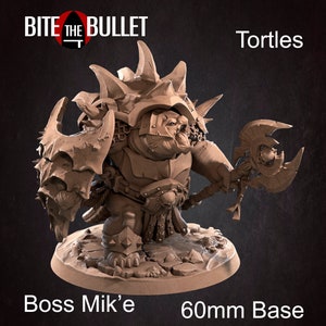 May include: A brown Tortles figurine, Boss Mik'e, with a 60mm base. The figure is heavily armored, holding a large axe and shield. The figure has a spiky shell and is posed on a circular base. The Bite the Bullet logo is in the upper left.