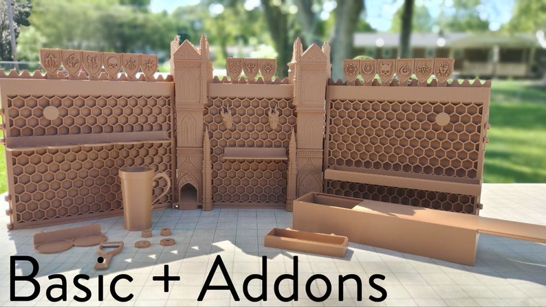 May include: A set of brown 3D printed castle walls with a honeycomb design and various accessories, including a mug, a small box, and a few other pieces. The text "Basic + Addons" is printed on the table in front of the castle walls.