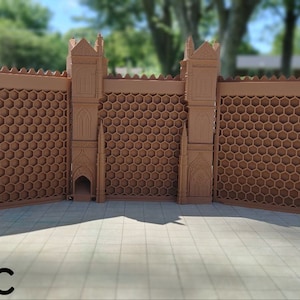 May include: A brown, 3D printed castle wall with a honeycomb pattern and two towers. The wall is made of multiple sections that can be connected together. The text "Basic" is printed on the ground in front of the wall.