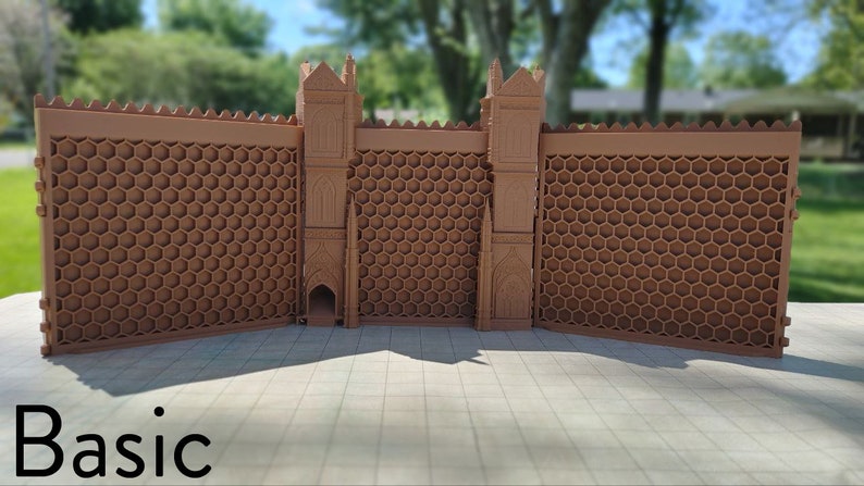 May include: A brown, 3D printed castle wall with a honeycomb pattern and two towers. The wall is made of multiple sections that can be connected together. The text "Basic" is printed on the ground in front of the wall.