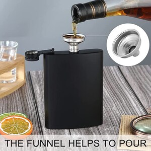May include: A black stainless steel hip flask with a silver funnel. The funnel is being used to pour liquid into the flask. The flask has a screw-on cap with a small silver loop.