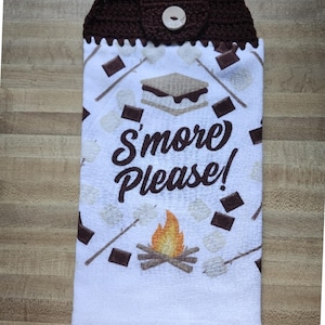 May include: A white kitchen towel featuring a brown crochet top with a button closure. The towel displays a pattern of s'mores, marshmallows on sticks, and a campfire, with the text S'more Please! printed in brown in the center of the fabric.