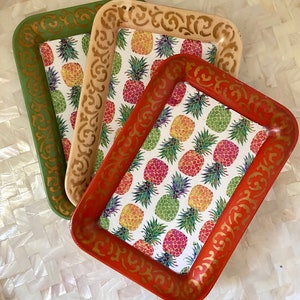 May include: Three rectangular trays with gold trim and a pineapple pattern. The trays are nested, with the largest tray on the bottom and the smallest tray on top. The trays are on a white surface.