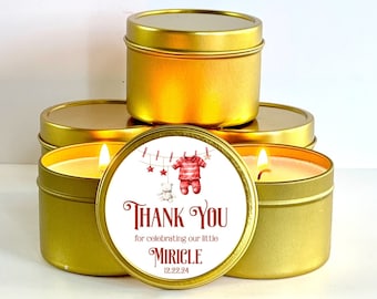 Op de afbeelding: Gouden blikje met kaars en een wit label met de tekst "Bedankt voor het vieren van onze kleine Miracle 12.22.24". Het label toont ook een rood-wit gestreepte baby-outfit die aan een waslijn hangt met een teddybeer en sterren.