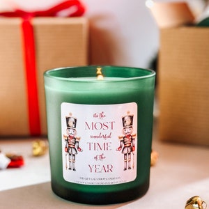 May include: Green glass candle with a white label that says "It's the most wonderful time of the year." The label features a watercolor illustration of two nutcracker soldiers.