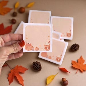 Pu&ograve; includere: Un foglietto adesivo quadrato con sfondo color pesca chiaro, caratterizzato da un bordo con zucche arancioni, una piccola candela e una tazza di caff&egrave; con panna montata. Il centro &egrave; vuoto per scrivere ed &egrave; decorato con piccole stelle.
