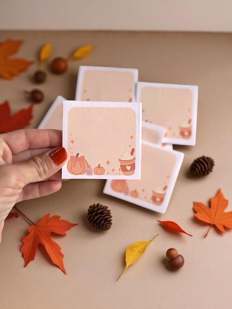 Pu&ograve; includere: Un foglietto adesivo quadrato con sfondo color pesca chiaro, caratterizzato da un bordo con zucche arancioni, una piccola candela e una tazza di caff&egrave; con panna montata. Il centro &egrave; vuoto per scrivere ed &egrave; decorato con piccole stelle.