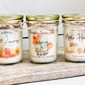 Peut inclure: Trois bougies en soja de 8 onces dans des pots en verre avec des couvercles dor&eacute;s et de la ficelle. Les bougies sont &eacute;tiquet&eacute;es "Fall Leaves", "Pumpkin Spice Latte" et "Apple Harvest". Chaque &eacute;tiquette pr&eacute;sente une illustration aquarelle et le texte "The Gift Gala Shop".