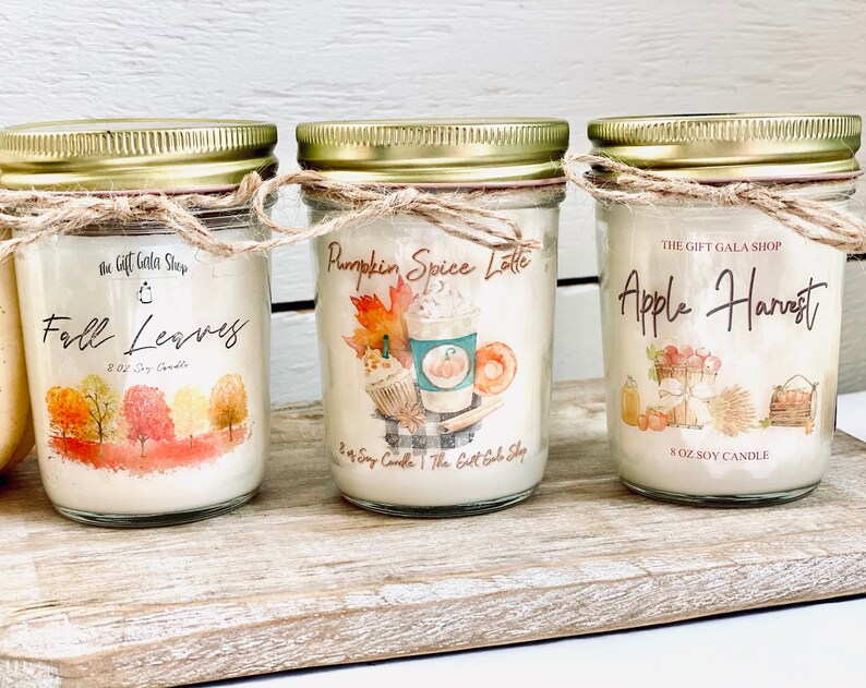 Peut inclure: Trois bougies en soja de 8 onces dans des pots en verre avec des couvercles dor&eacute;s et de la ficelle. Les bougies sont &eacute;tiquet&eacute;es "Fall Leaves", "Pumpkin Spice Latte" et "Apple Harvest". Chaque &eacute;tiquette pr&eacute;sente une illustration aquarelle et le texte "The Gift Gala Shop".