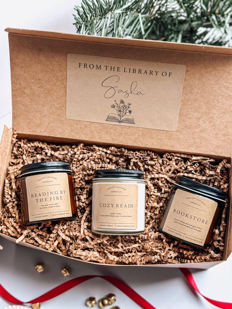 May include: A brown box with a label that says "From the Library of Sasha" and contains three candles. The candles are labeled "Reading by the Fire", "Cozy Reads", and "Bookstore".